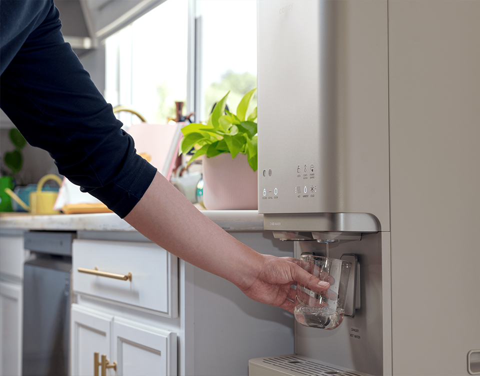 Coway tankless water purifier installed in a home kitchen, dispensing a glass of water
